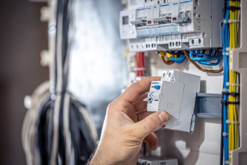 A male electrician works in a switchboard with an electrical connecting cable.